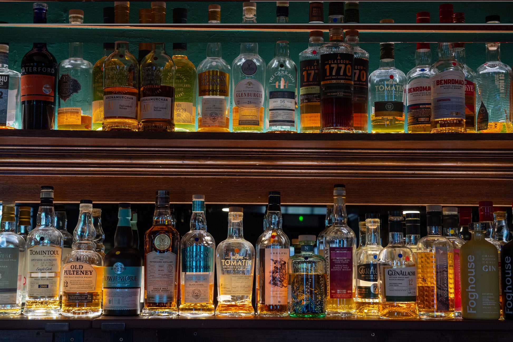 Row of whiskey bottles on a bar shelf with a dark background
